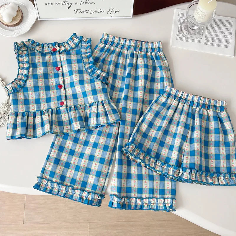Blue and white checkered children's outfit on a white surface with a candle and paper in the background.