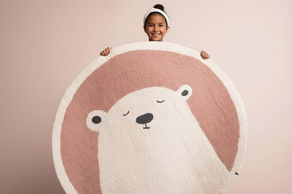 Person holding a round rug with a bear design on a pink background