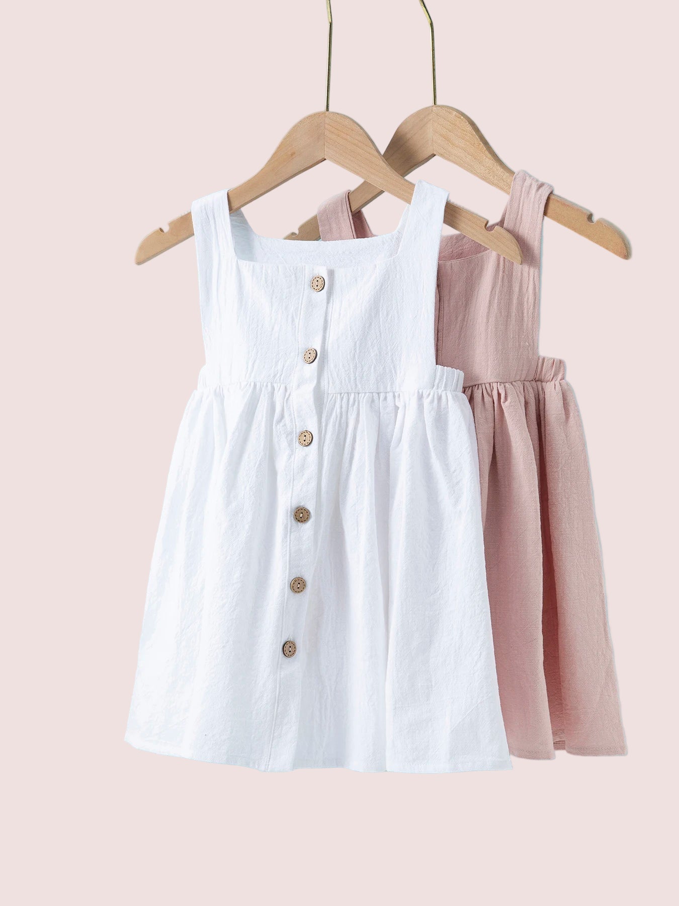 Two dresses, one white and one pink, hanging on wooden hangers against a light blue background.