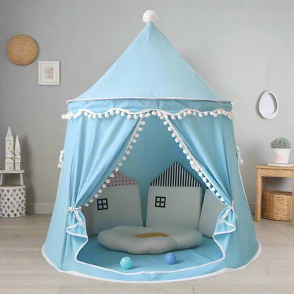 A beige Children's Bali Teepee Tent with a whimsical design, featuring pom-pom details and a small house shape on the front. The tent is set up indoors on a white carpet.