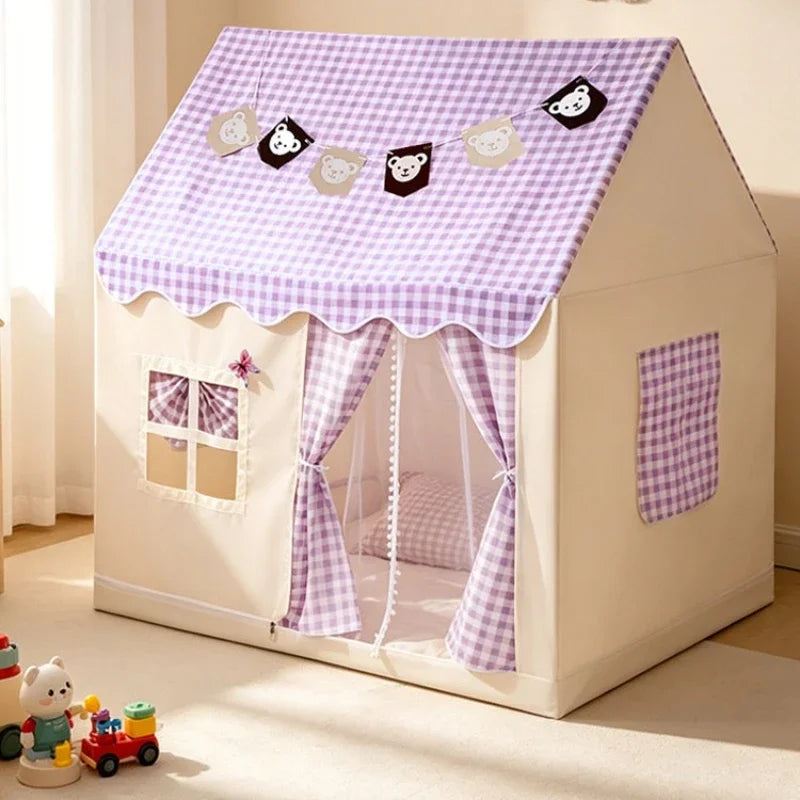 A children's playhouse tent with a beige body and a purple-and-white gingham fabric roof, curtains, and side pocket, decorated with a small bear banner on the roof. It is photographed in a softly lit room with toys on the floor nearby.