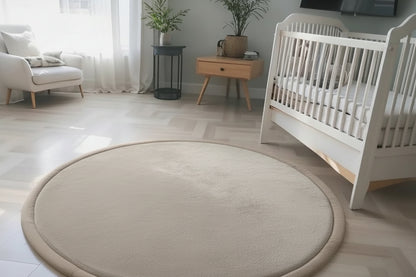 Round rug in a nursery with toys on it, surrounded by a white crib and a white armchair.